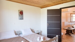 Quarto de hotel com duas camas, teto de madeira, guarda-roupa preto, uma pequena mesa com uma tigela e uma cadeira.