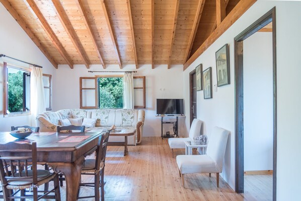 Una sala acogedora con vigas de madera, un sofá, una mesa de comedor y un televisor.