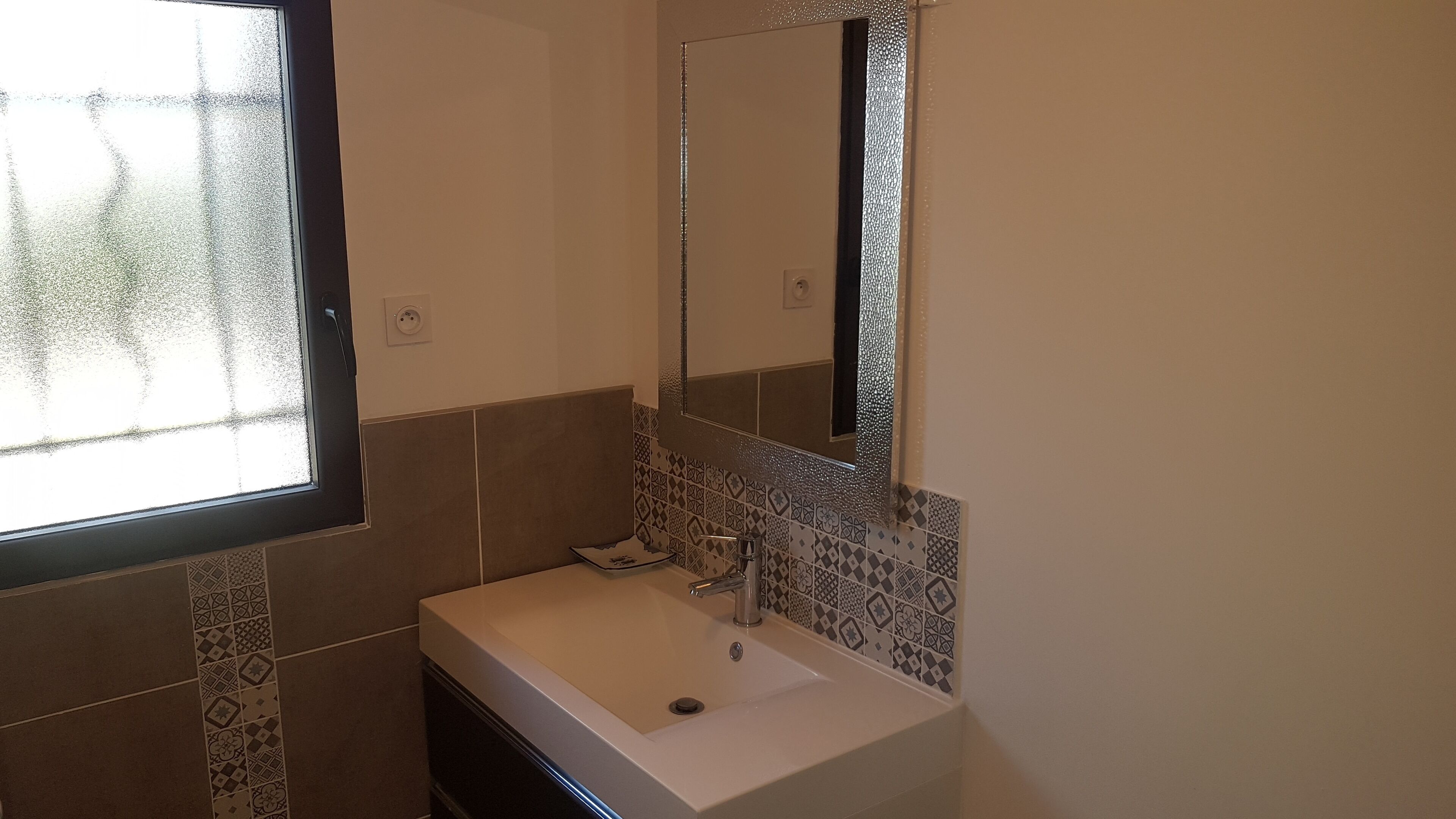 Une salle de bain avec un lavabo blanc, un miroir et des carreaux décoratifs sur les murs.