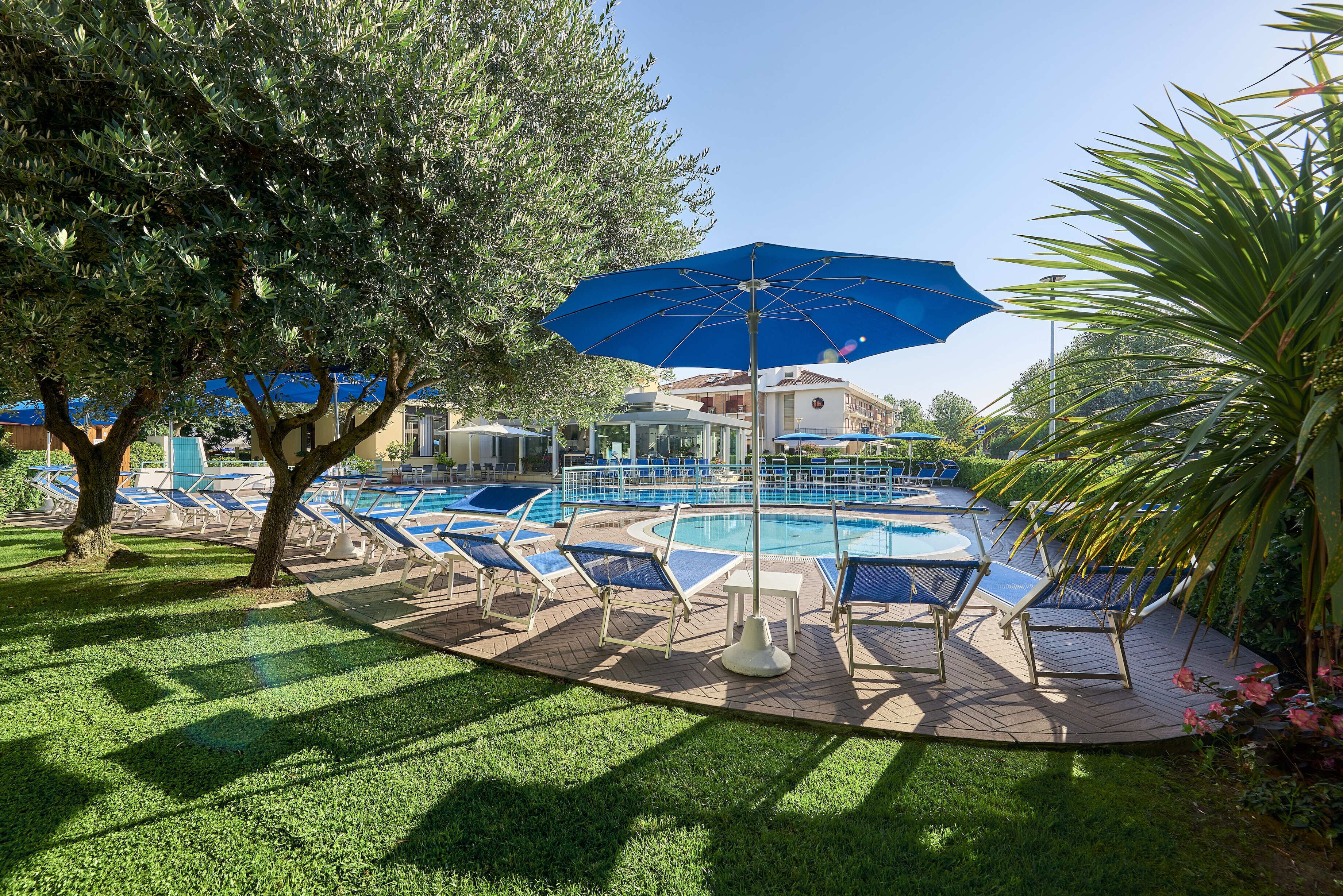 A swimming pool with lounge chairs and a large umbrella, surrounded by trees and a well-maintained lawn.