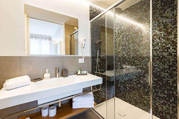Un baño moderno con un espejo grande, lavamanos blanco y cabina de ducha de vidrio.