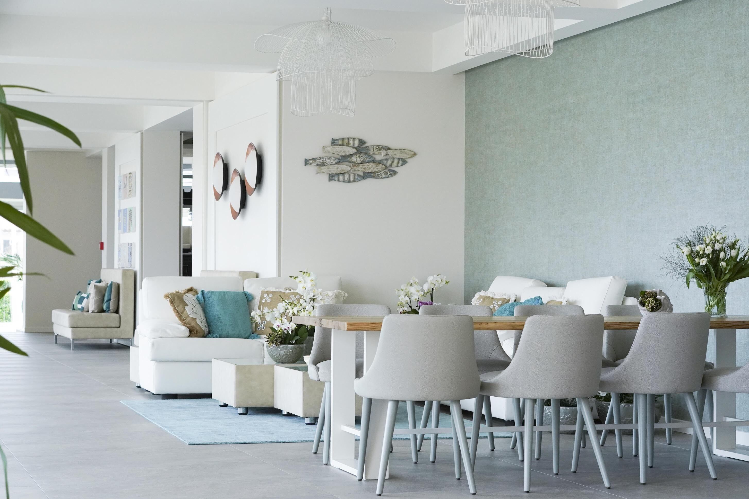 A modern living room with a dining area, featuring a white sofa, grey chairs, a wooden dining table, and decorative fish wall art.
