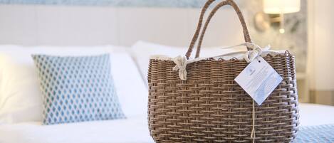 A wicker basket with a tag on a bed with patterned pillows.