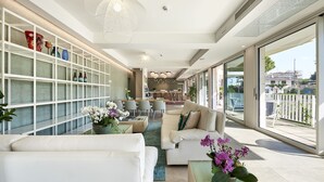 A modern living room with a sofa, coffee table, and a bookshelf filled with decorative items. - Junior Family Hotel (Cavallino-Treporti)
