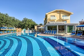 Una piscina con azulejos azules, sillas de descanso y un edificio con balcones.