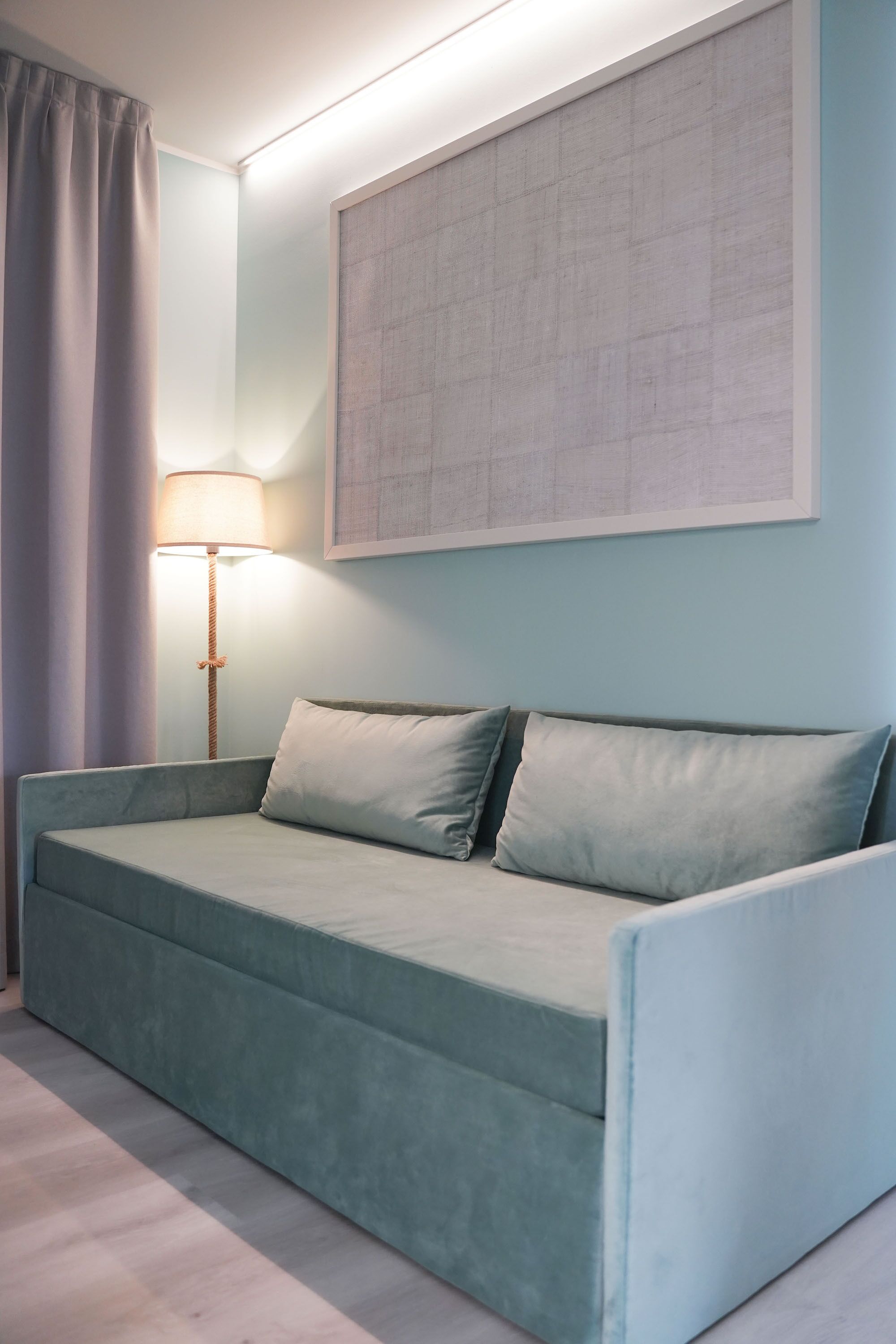 Ein hellblaues Sofa mit zwei Kissen, einer Stehlampe und einem großen abstrakten Gemälde an der Wand.