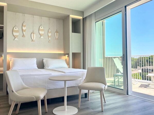 Een hotelkamer met een bed, twee stoelen, een tafeltje en een balkon met uitzicht.