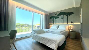 Habitación de hotel con dos camas, una silla, una mesita y un balcón con vistas.