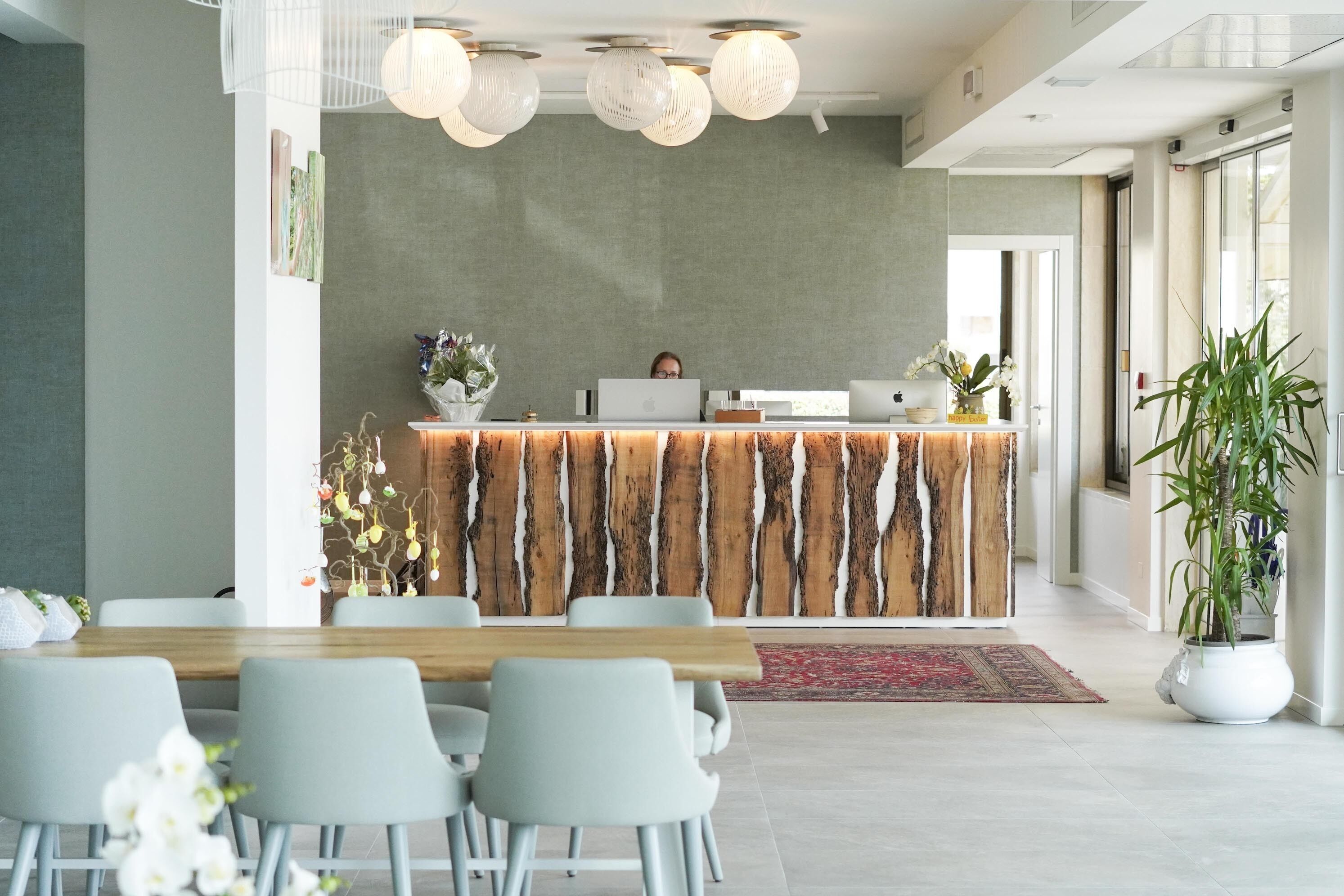 A modern reception area with a wooden reception desk, multiple chairs, and a large potted plant.