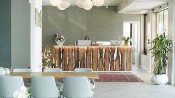 A modern reception area with a wooden reception desk, multiple chairs, and a large potted plant.