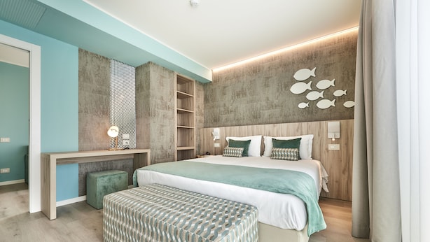 A modern bedroom with a bed, bedside tables, a bench, and a wall with fish decorations. - Junior Family Hotel (Cavallino-Treporti)
