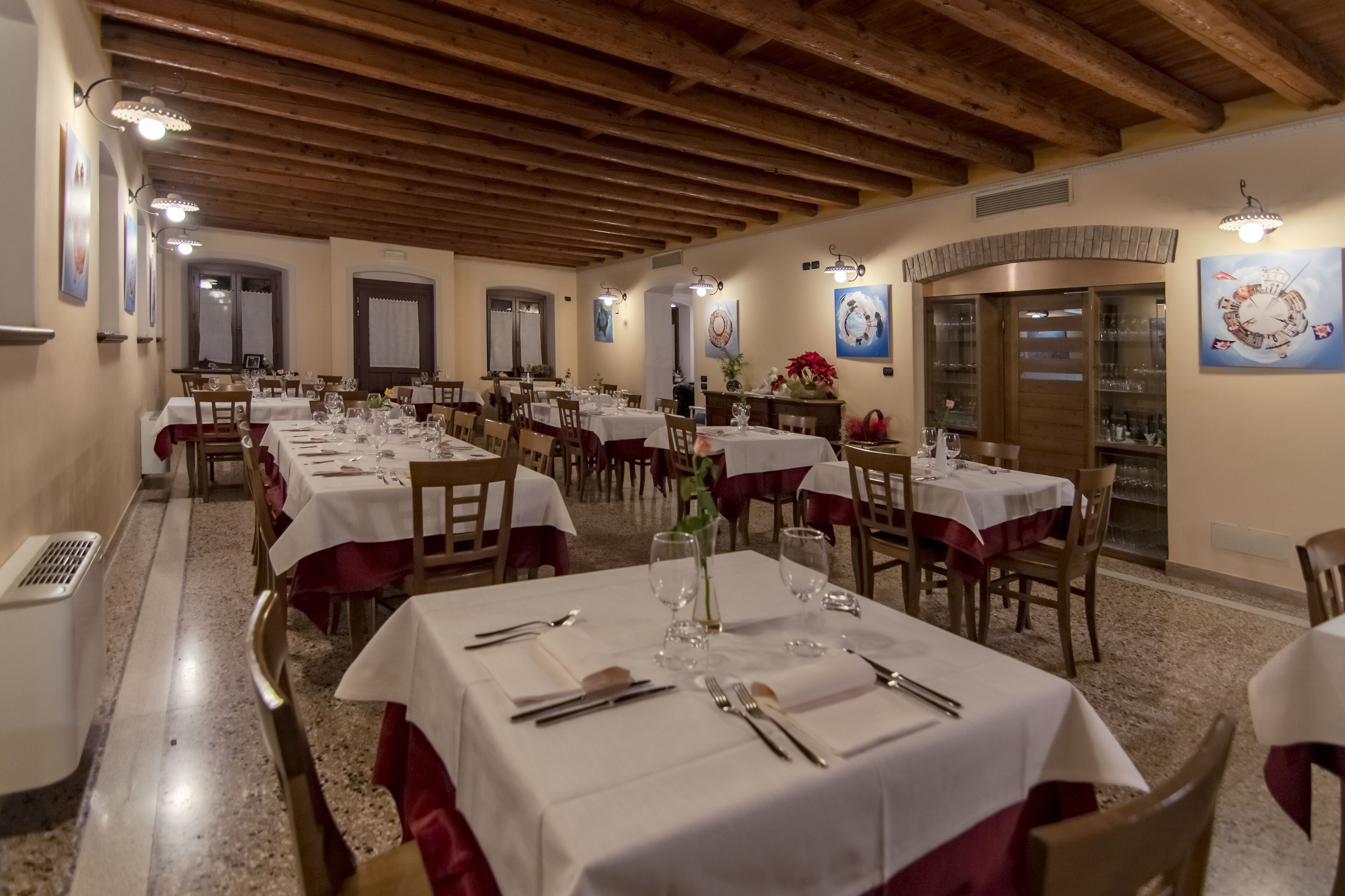 A restaurant with multiple tables set for dining, wooden beams on the ceiling, and artwork on the walls.