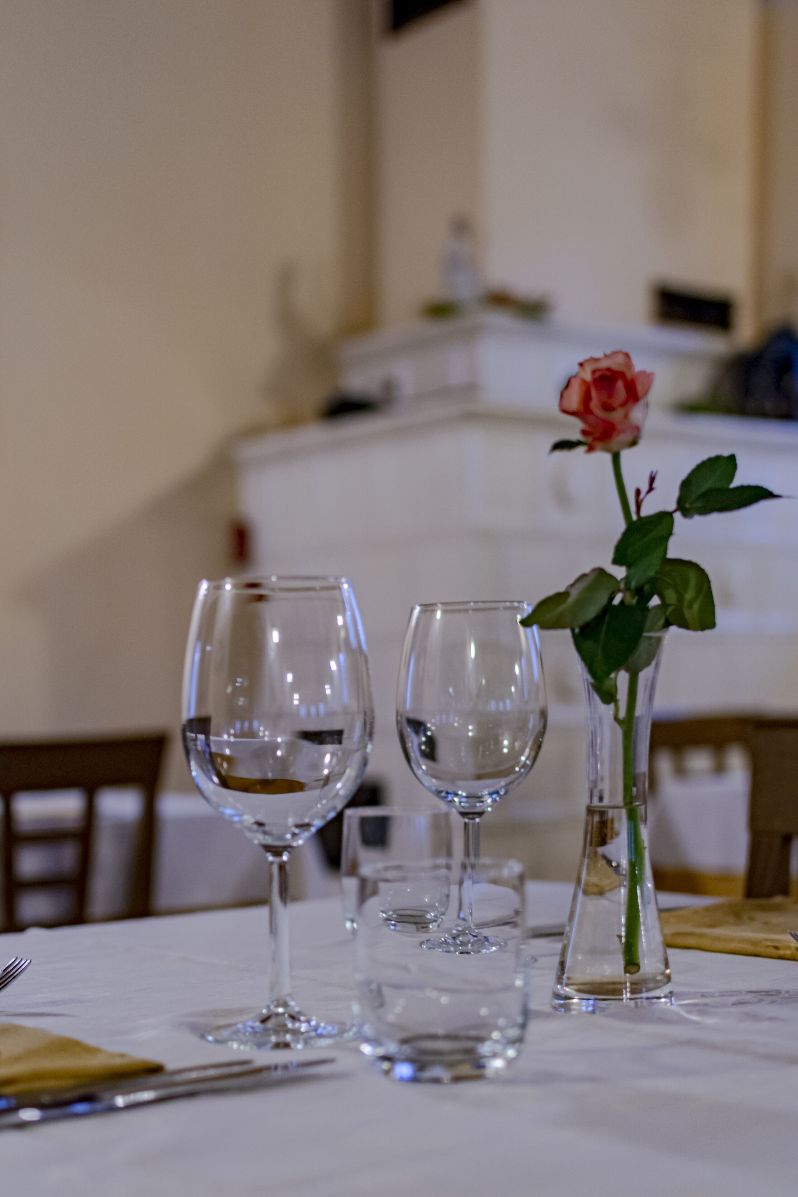 Una mesa de comedor con dos copas de vino y un jarrón con una rosa.