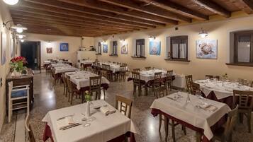 A restaurant with multiple tables set for dining, wooden beams on the ceiling, and wall-mounted artwork.