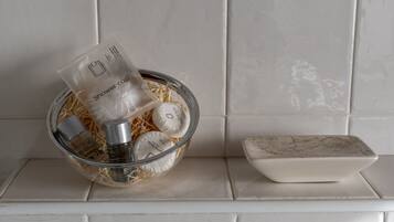 A bathroom with a glass bowl containing toiletries, a shower cap, and a soap dispenser on a tiled shelf.