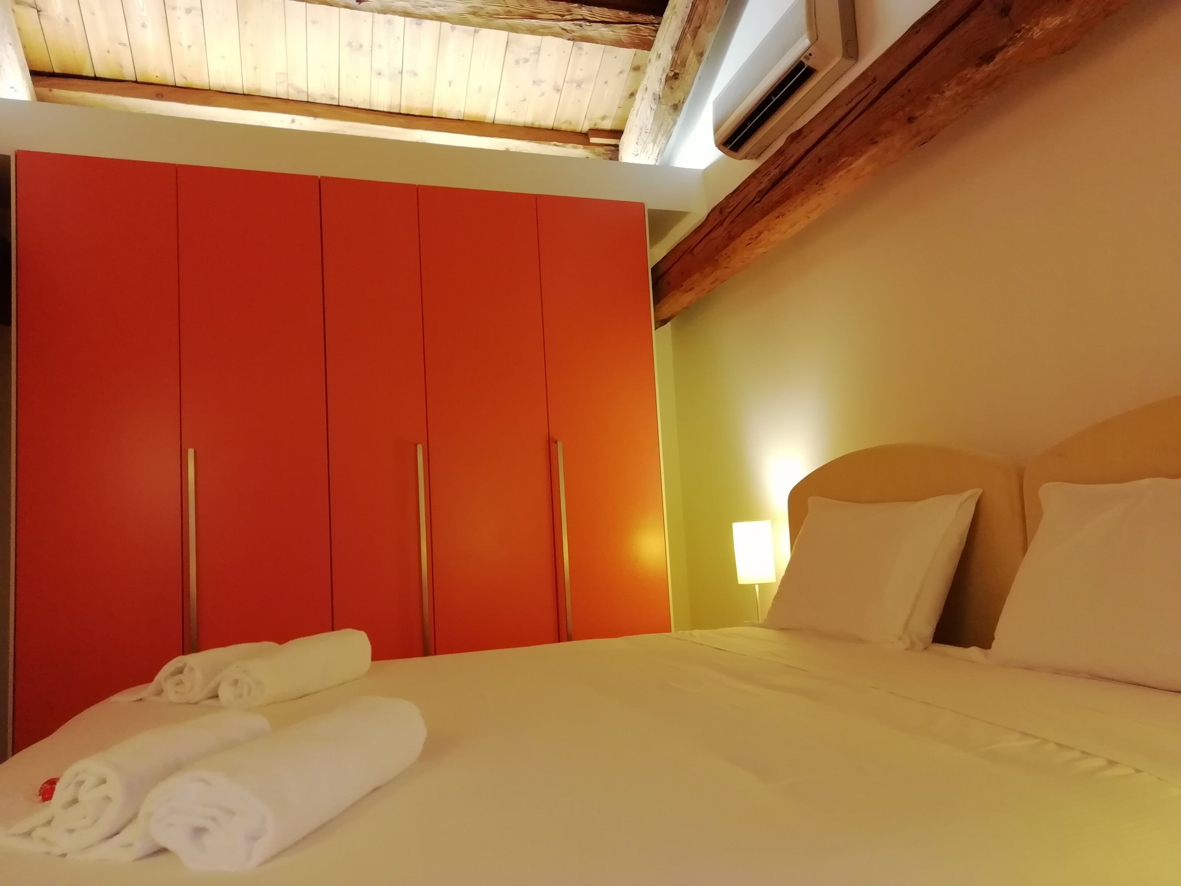 A hotel room with a bed, a red wardrobe, and a ceiling with wooden beams.