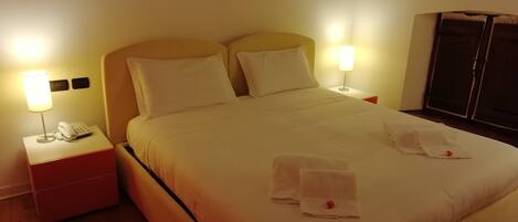 A neatly made bed with white linens, two bedside lamps, a bedside phone, and a red object on the bed.