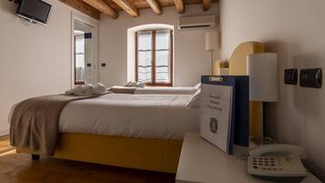 A hotel room with a bed, a bedside table with a phone, a lamp, and a window with curtains.