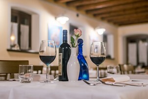 Una mesa de comedor dispuesta con copas de vino, una botella y un florero con una rosa.