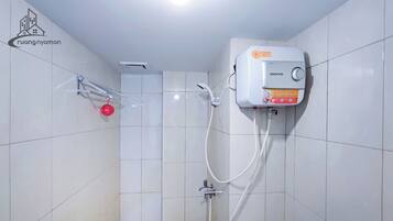 Une salle de bain avec des murs carrelés de blanc, une douche équipée d’un pommeau de douche à main et un chauffe-eau mural portant l’inscription « Domo ».