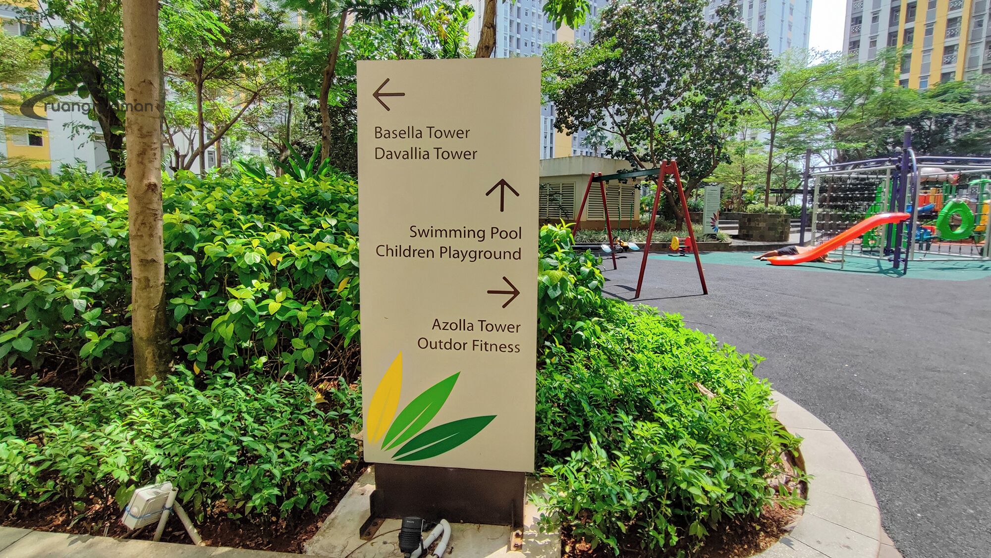 Un letrero direccional con flechas que indican varios servicios, como piscina, parque infantil y zona de fitness al aire libre.