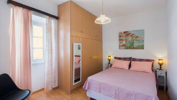 A bedroom with a bed, a chair, a wardrobe, a painting, and a window with curtains.