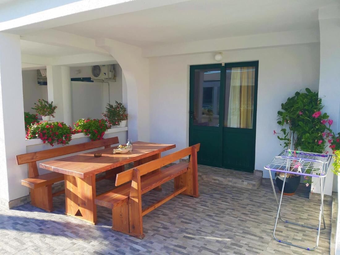 An outdoor wooden table and benches, a green door, and a metal drying rack with plants.