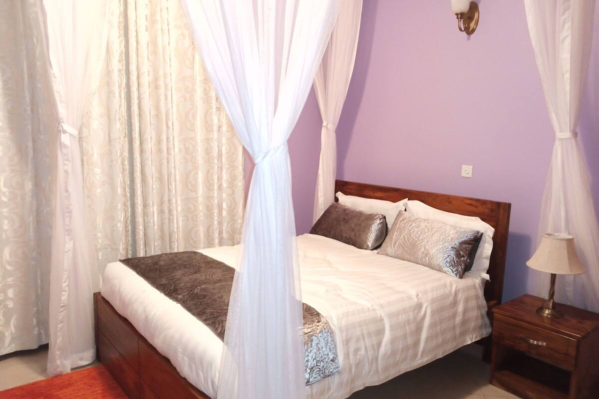 A bedroom with a bed, curtains, a nightstand, and a wall-mounted lamp.