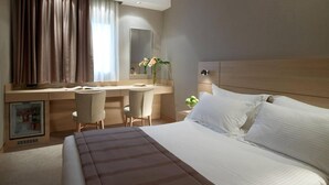 Hotellihuoneessa on sänky, työpöytä, kaksi tuolia, peili ja pieni jääkaappi.