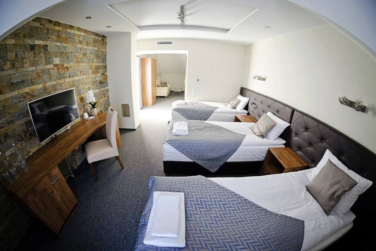 Quarto de hotel com parede de pedra, duas camas, uma TV, uma escrivaninha e uma cadeira.