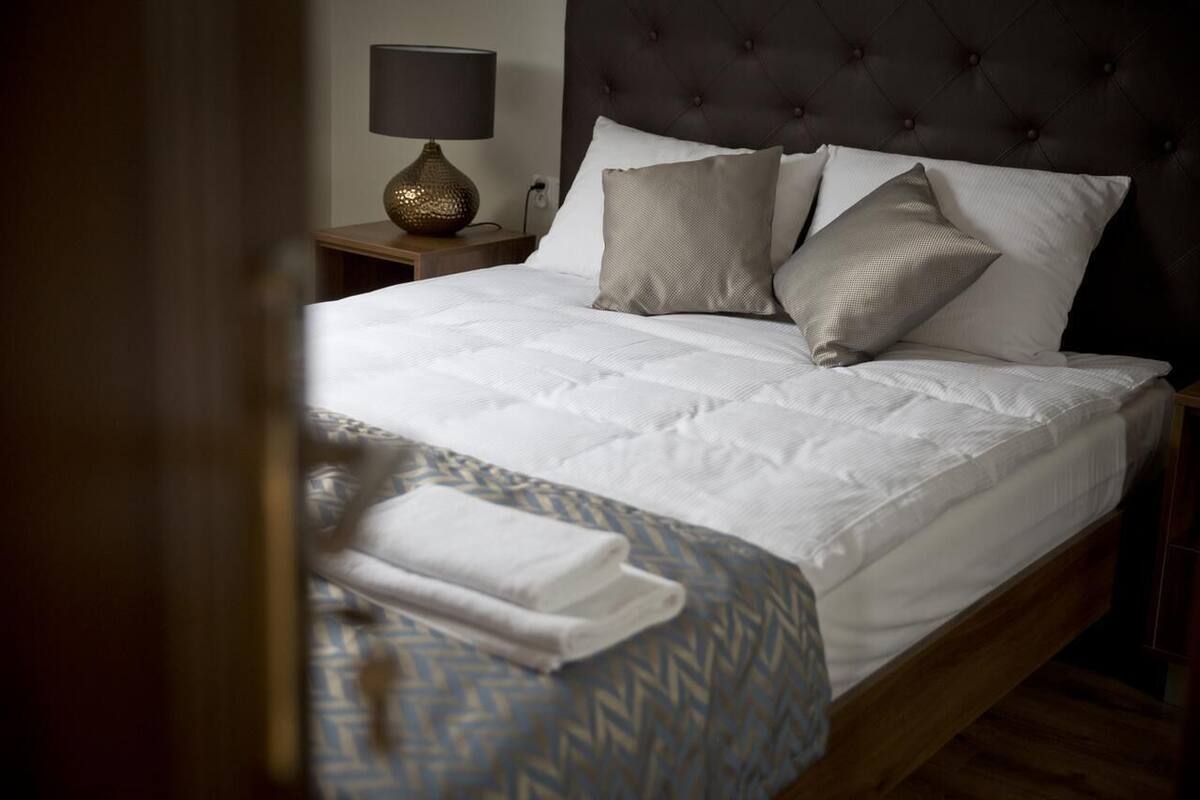 Uma cama bem arrumada com colcha estampada e travesseiros, um abajur e uma cabeceira acolchoada escura.