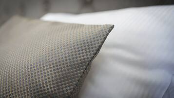 A close-up of a textured pillow with a geometric pattern, part of a bed with a white pillow and a grey headboard.