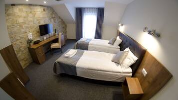 Quarto de hotel com duas camas, uma escrivaninha, televisão e uma parede de pedra.