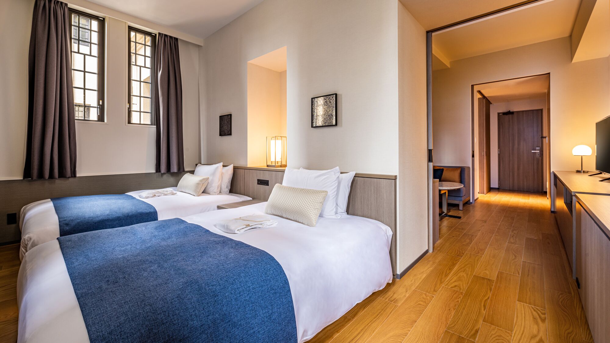 A hotel room with two beds, a desk, a chair, and a TV.