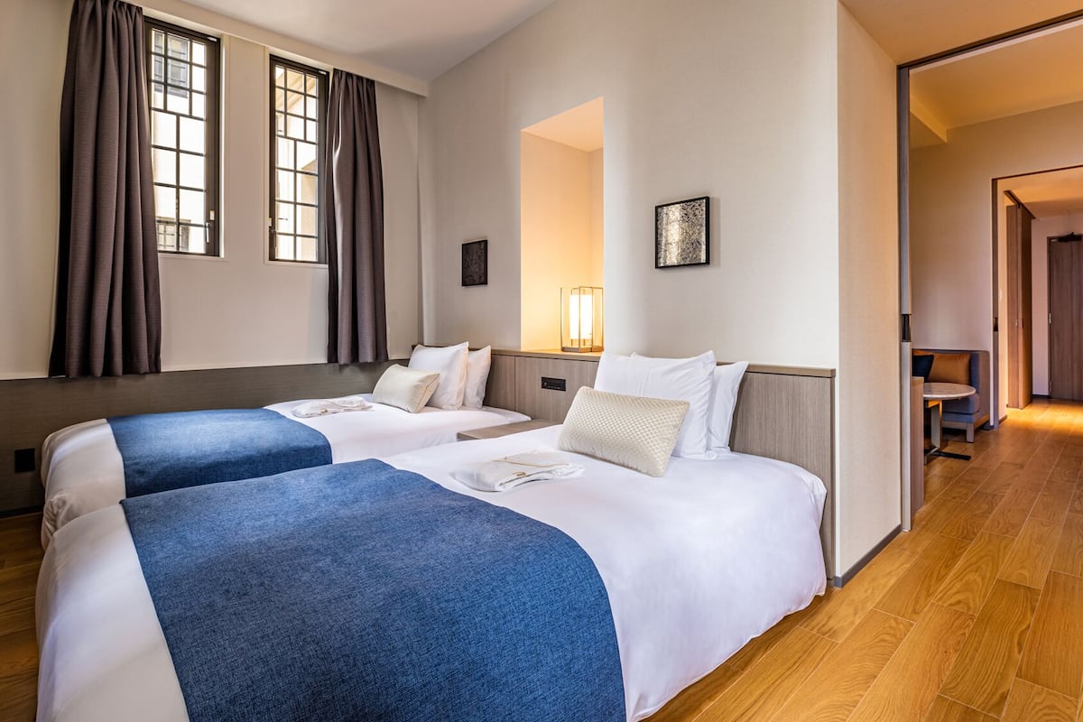 A hotel room with two beds, a desk, a chair, and a TV.