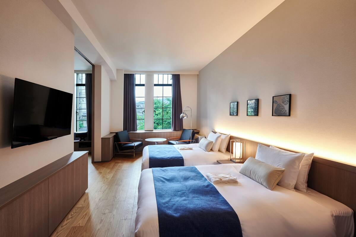 Habitación de hotel con dos camas, televisión, escritorio y ventana con cortinas.