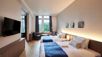 A hotel room with two beds, a TV, a desk, and a window with curtains.