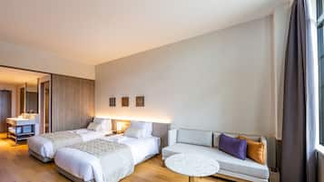 A hotel room with two beds, a sofa, a round table, and a bathroom with a mirror and sink.