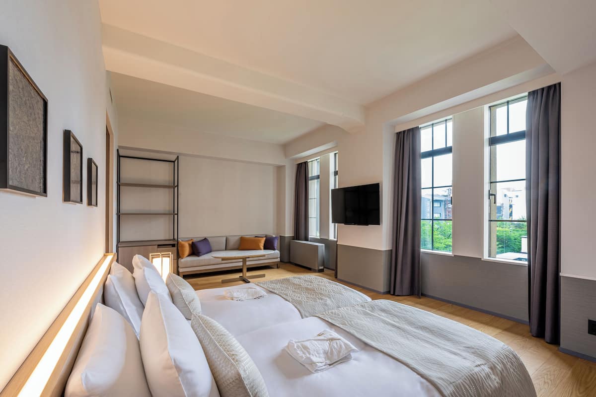 A modern hotel room with a large bed, a sofa, a TV, and large windows.
