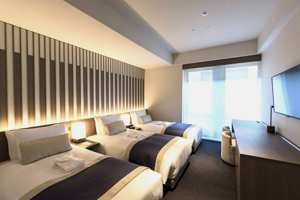 Habitación de hotel con dos camas, un escritorio y televisión.