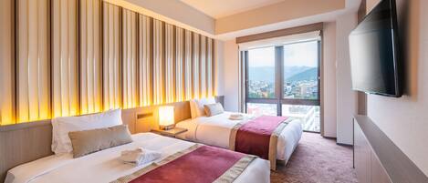 A hotel room with two beds, a large window with a city view, a flat-screen TV mounted on the wall, and a wooden headboard.