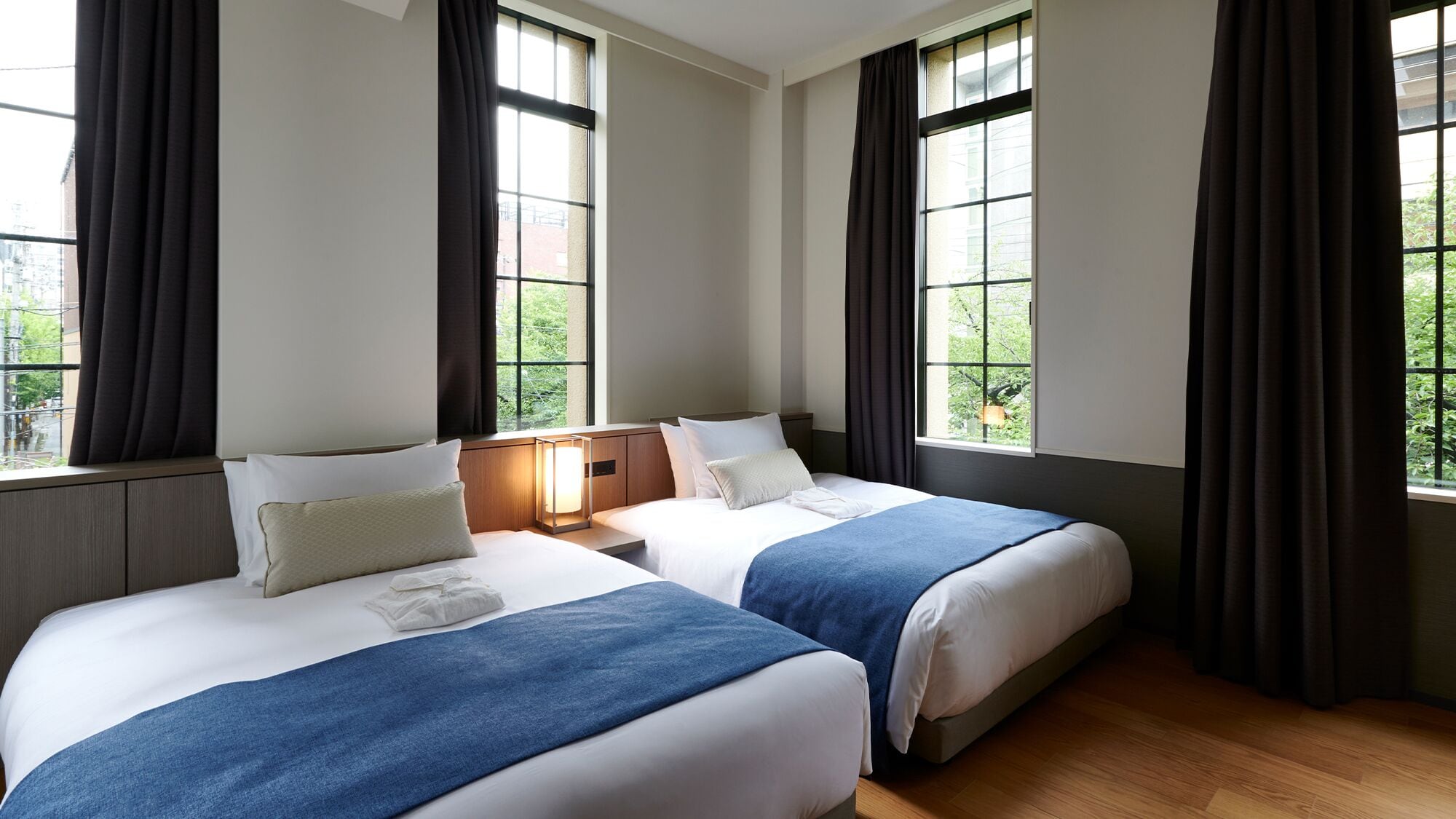 A hotel room with two beds, large windows, and a view of greenery.