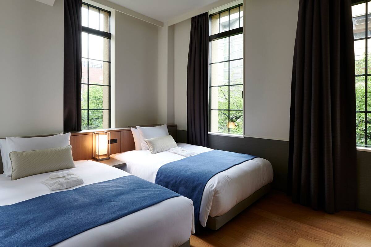 A hotel room with two beds, large windows, and a view of greenery.