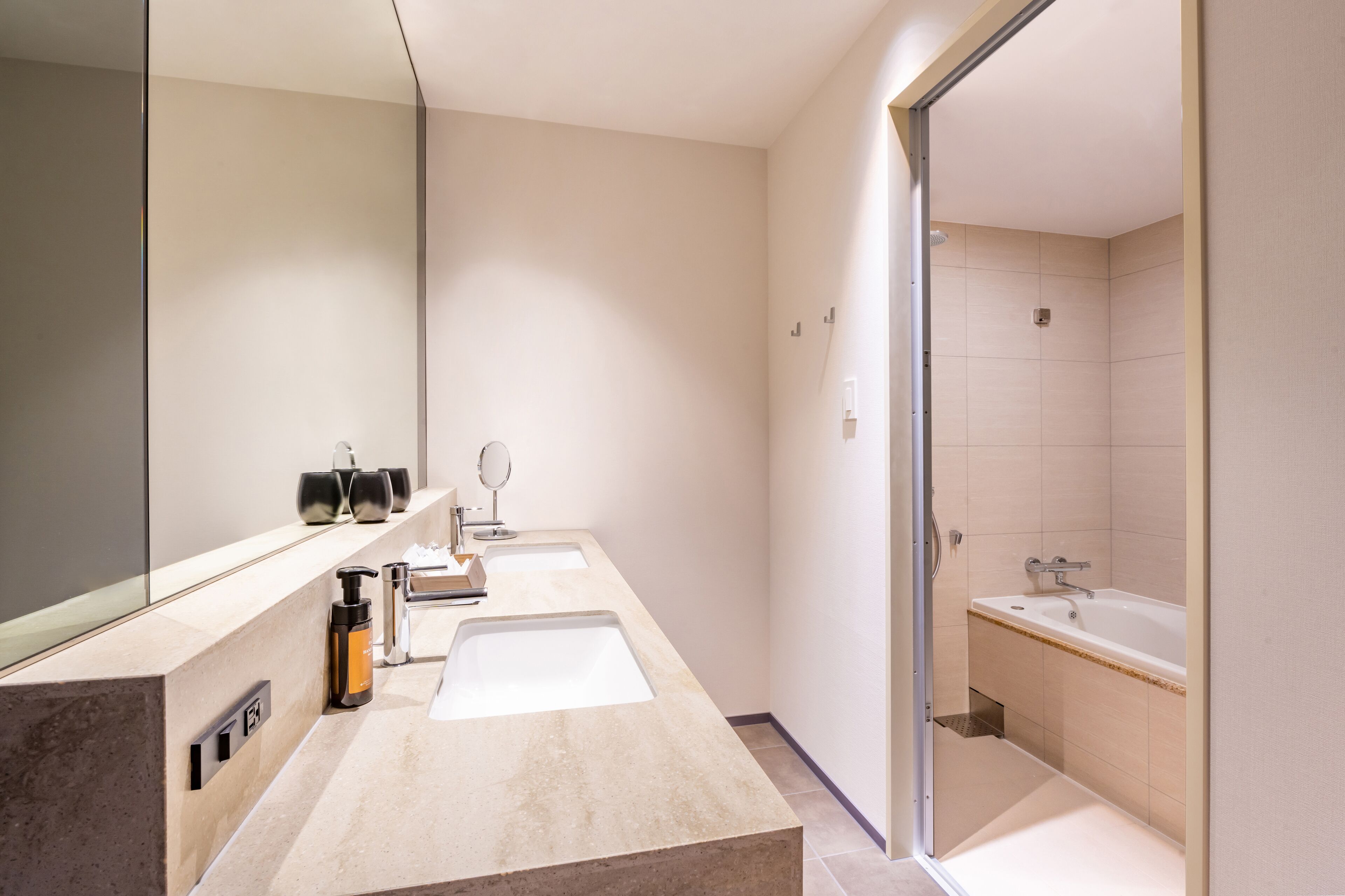 A modern bathroom with two sinks, a large mirror, and a bathtub.