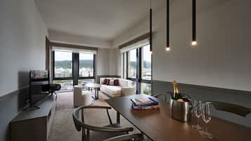 Una sala de estar moderna con una mesa de madera, libros, una botella de champán y copas de vino. Cuenta con un sofá, un televisor y ventanas amplias con vistas a la ciudad.