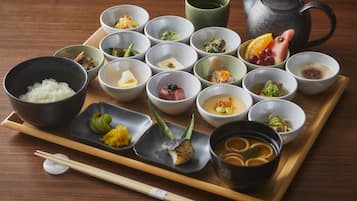 A tray with various bowls of food, a teapot, and chopsticks on a wooden table.