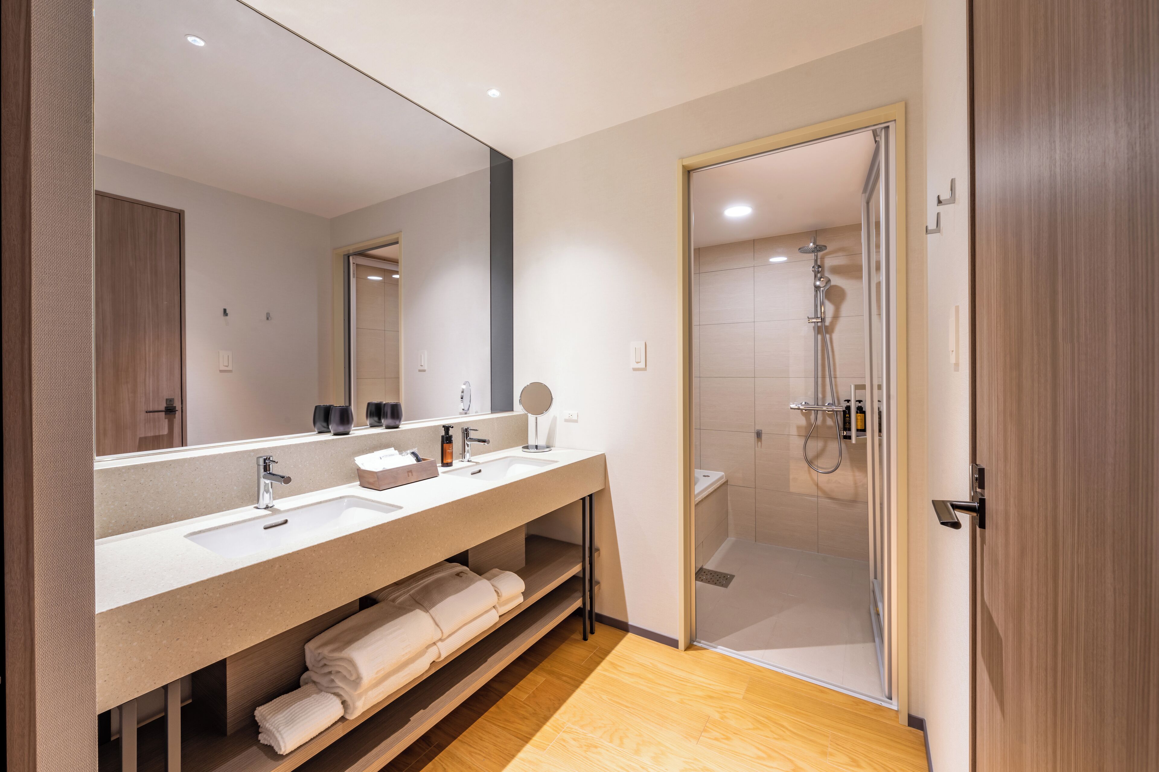 Un baño moderno con un espejo grande, dos lavamanos, una ducha y piso de madera.