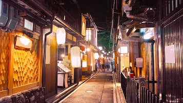 A narrow street with traditional wooden buildings, illuminated signs, and a stone pathway.