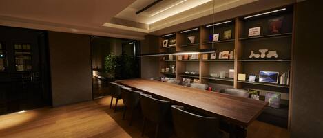 A modern dining area with a long wooden table, several chairs, and built-in bookshelves with various items.