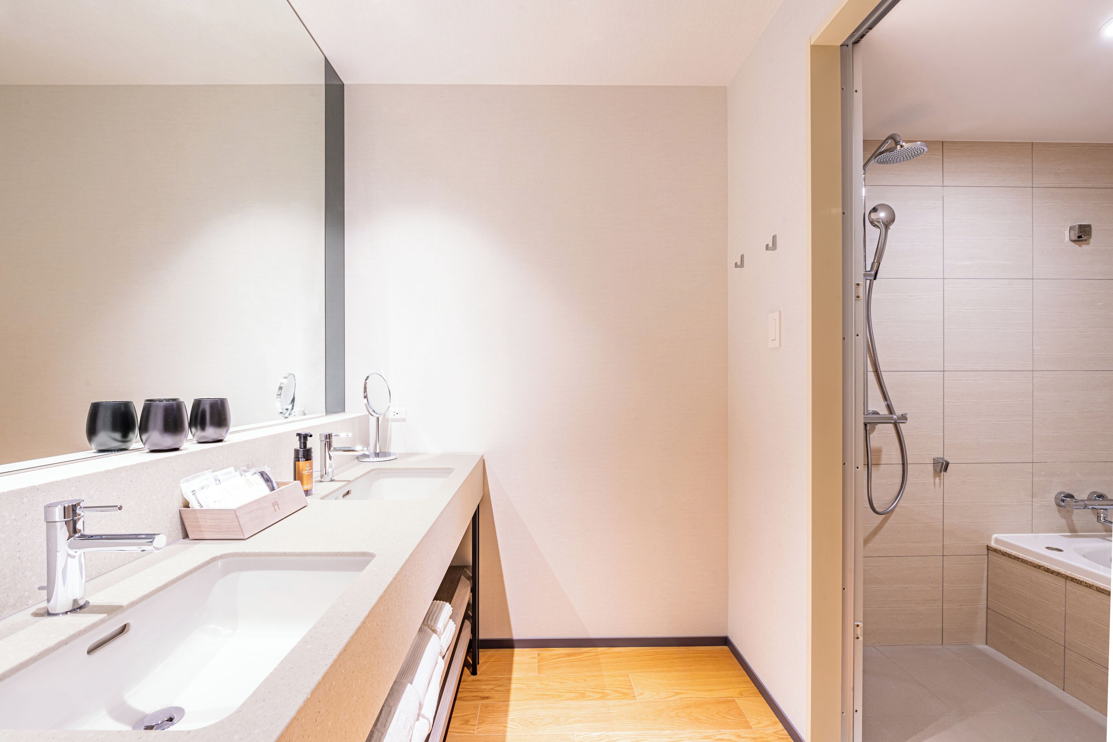 A modern bathroom with two sinks, a shower, and a large mirror.